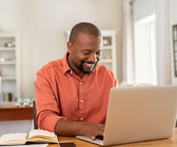 Photo of a smiling man while facing on his laptop